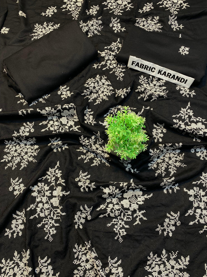 The black fabric adorned with white floral embroidery is presented, highlighted by a small green plant at its center. In the upper right corner, a label reveals "Regal Hues Bareeze" from ESHMEEN's Winter Collection, emphasizing its premium quality.