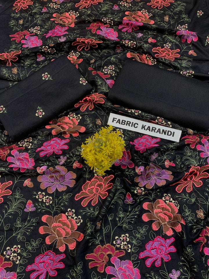 A spread labeled Bareeze Royal Flame from the ESHMEEN brand features intricate floral embroidery in pink, red, and green on a blue background. Two folded pieces of solid blue fabric rest on top, accented with a small green decorative plant—ideal for your Premium Quality Winter Collection.