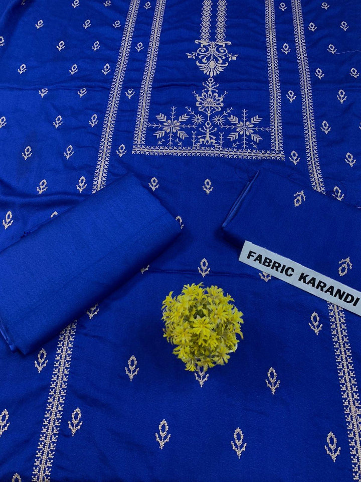 Regal Dusk Bareeze from ESHMEEN showcases beautifully intricate blue patterns on purple fabric, with two artfully folded pieces labeled as part of the Winter Collection. A small yellow bouquet is elegantly placed at the center on this premium quality fabric.