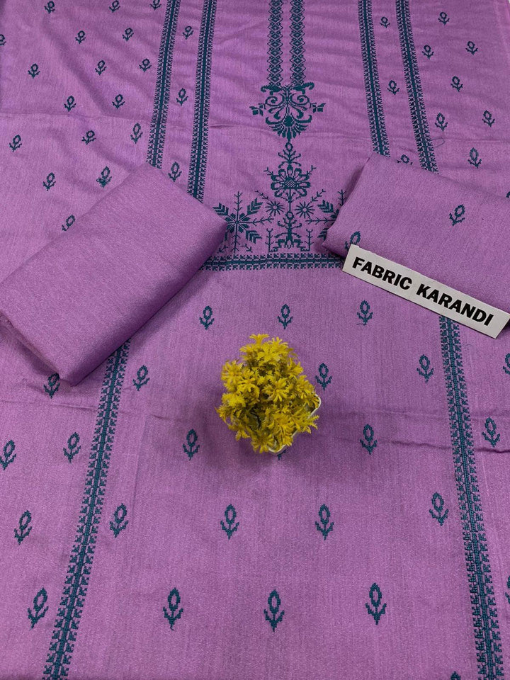 Regal Dusk Bareeze from ESHMEEN showcases beautifully intricate blue patterns on purple fabric, with two artfully folded pieces labeled as part of the Winter Collection. A small yellow bouquet is elegantly placed at the center on this premium quality fabric.