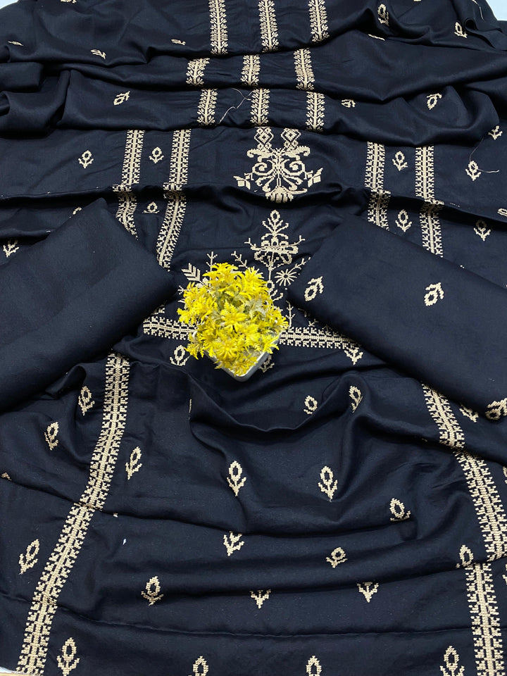 A blue fabric with intricate gold embroidery is spread out, showcasing its detailed design. A small green plant is placed on top, with a label reading Eternal Charm Bareeze from ESHMEEN's Winter Collection.