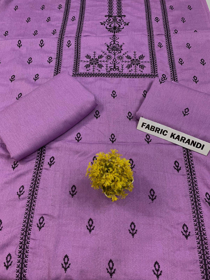 Regal Dusk Bareeze from ESHMEEN showcases beautifully intricate blue patterns on purple fabric, with two artfully folded pieces labeled as part of the Winter Collection. A small yellow bouquet is elegantly placed at the center on this premium quality fabric.