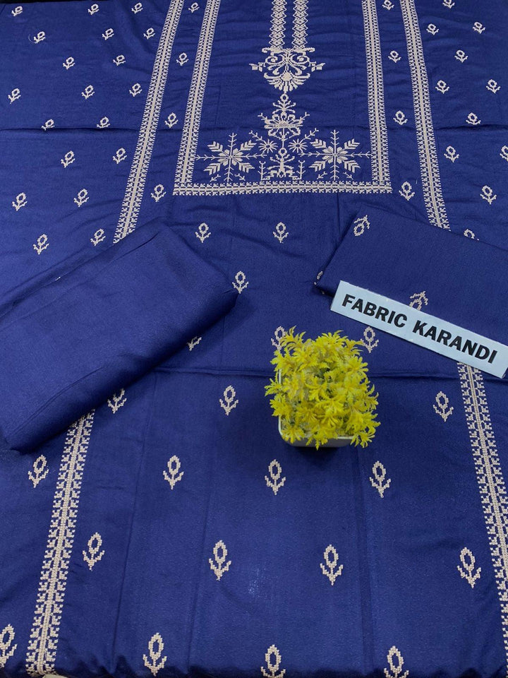 Regal Dusk Bareeze from ESHMEEN showcases beautifully intricate blue patterns on purple fabric, with two artfully folded pieces labeled as part of the Winter Collection. A small yellow bouquet is elegantly placed at the center on this premium quality fabric.