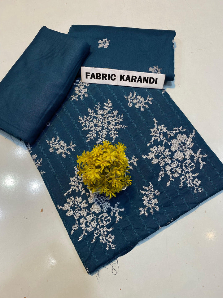 The black fabric adorned with white floral embroidery is presented, highlighted by a small green plant at its center. In the upper right corner, a label reveals "Regal Hues Bareeze" from ESHMEEN's Winter Collection, emphasizing its premium quality.